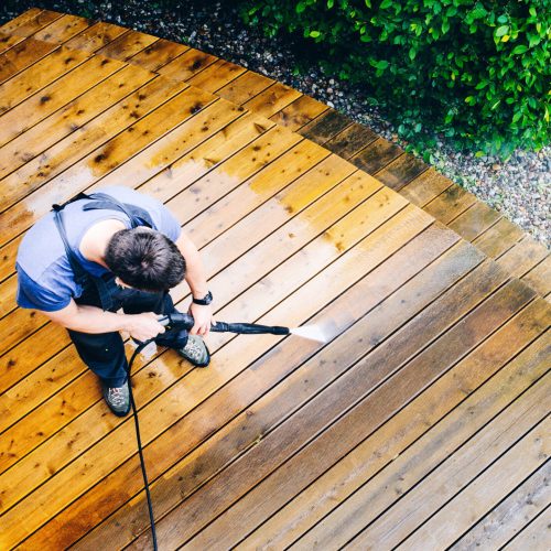 man cleaning terrace with a power washer - high water pressure cleaner on wooden terrace surface